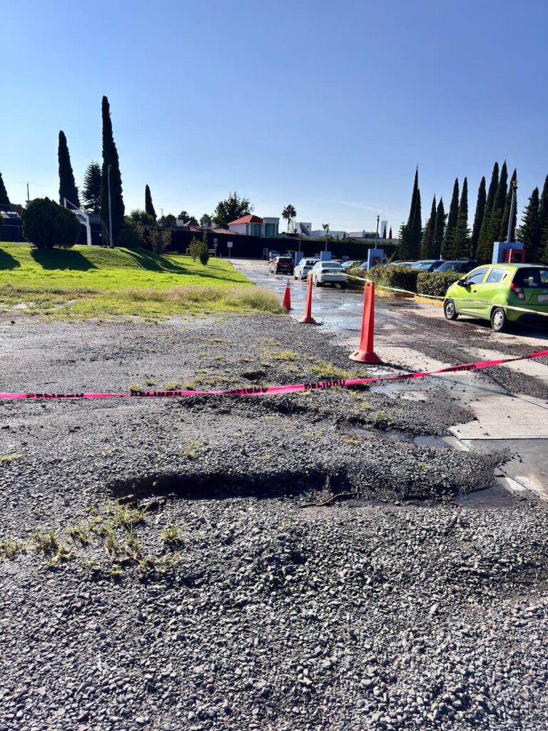 Entrada principal del estacionamiento de la UMAD con grava hundida y zonas irregulares causadas por las lluvias recientes.