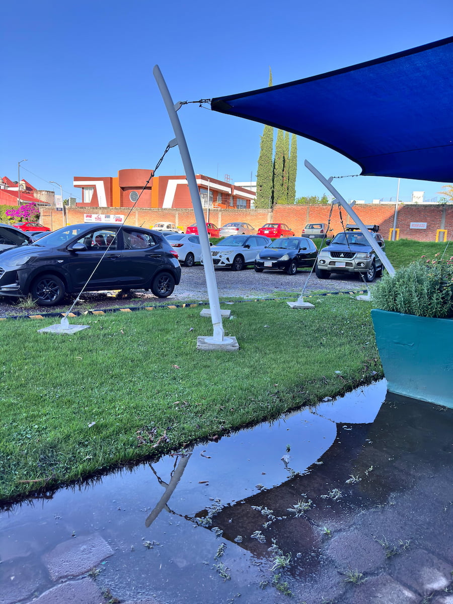 Vista general del estacionamiento de la UMAD cubierto de charcos y con el suelo de grava deteriorado por las lluvias.