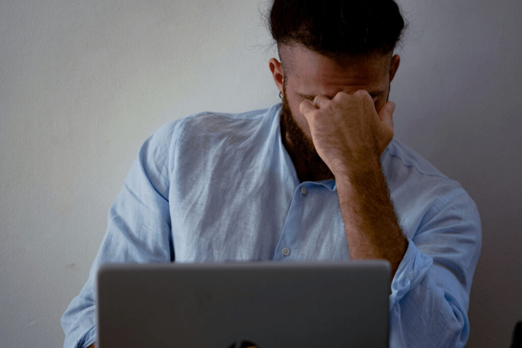 Un hombre universitario se cubre los ojos del cansancio mientras estudia frente a la computadora.